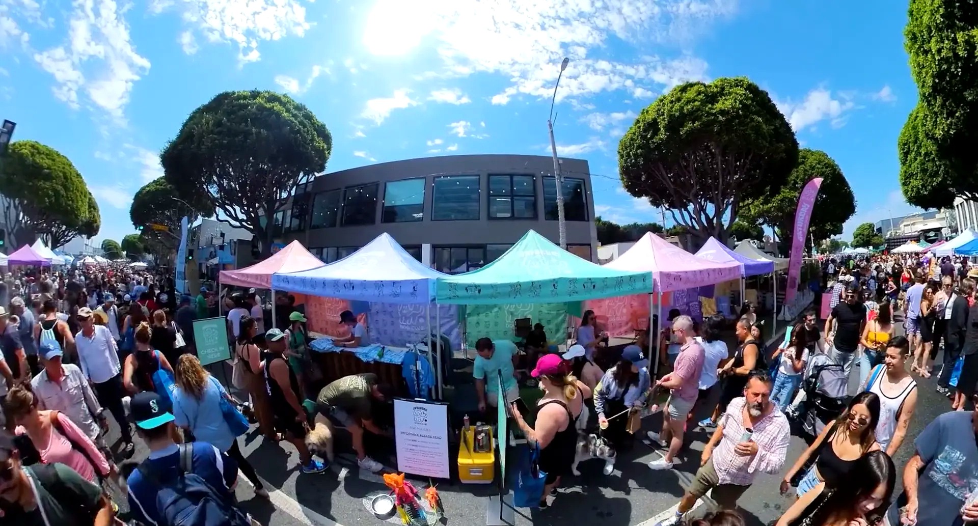 Wide view of the festival street lined with pastel tents and crowds under blue sky