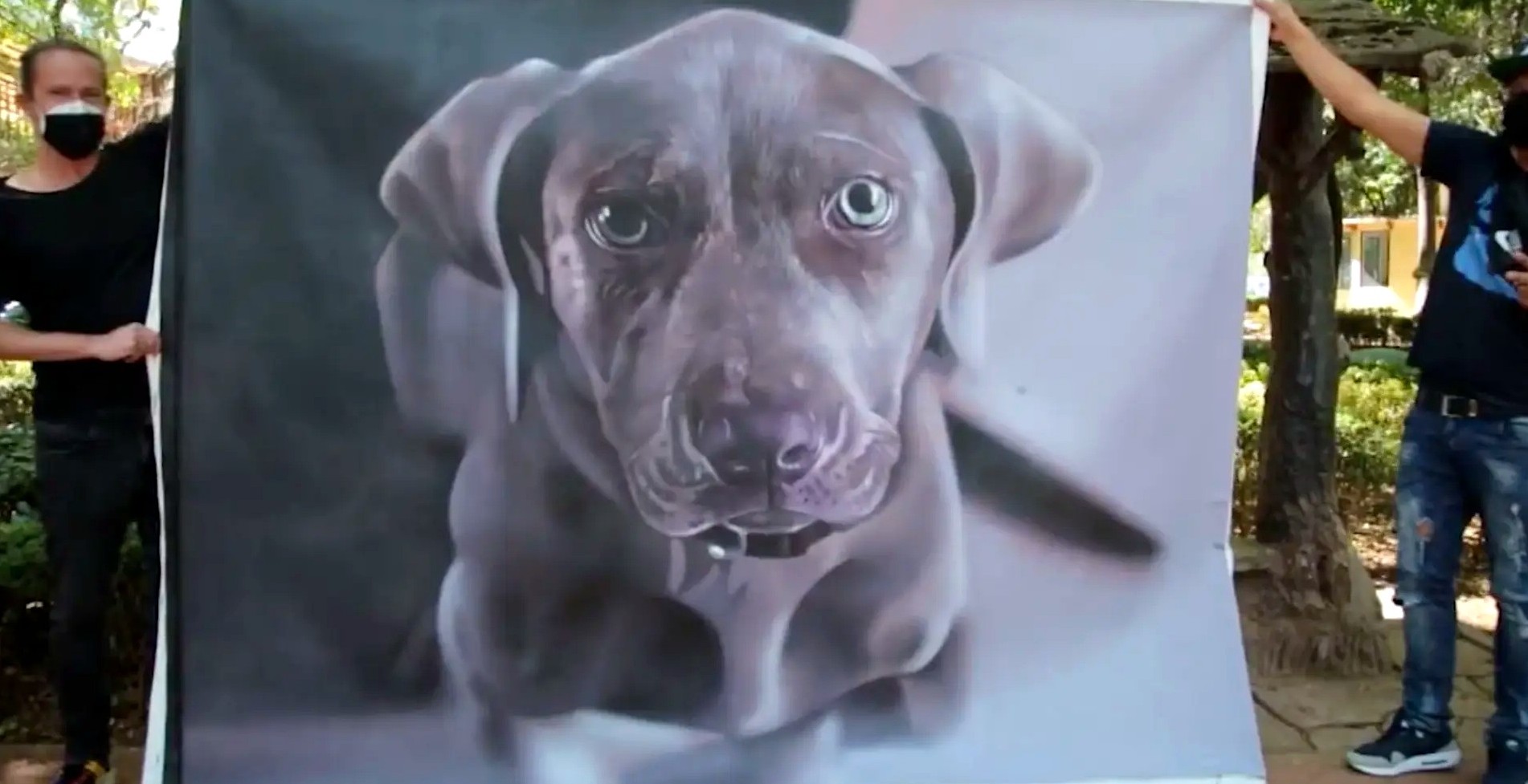 Two artists holding up a photorealistic airbrushed banner of a grey puppy