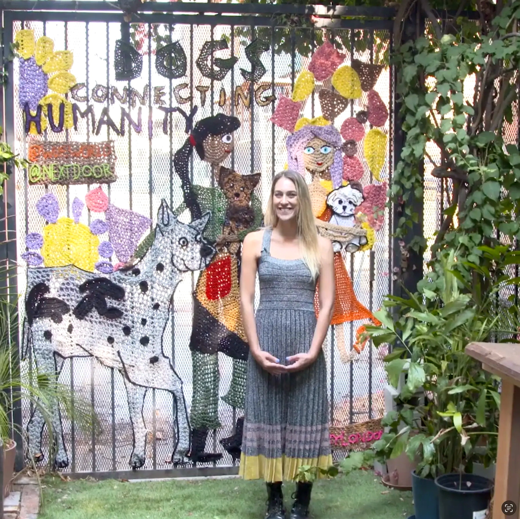Artist in front of a large crocheted installation reading Dogs Connecting Humanity