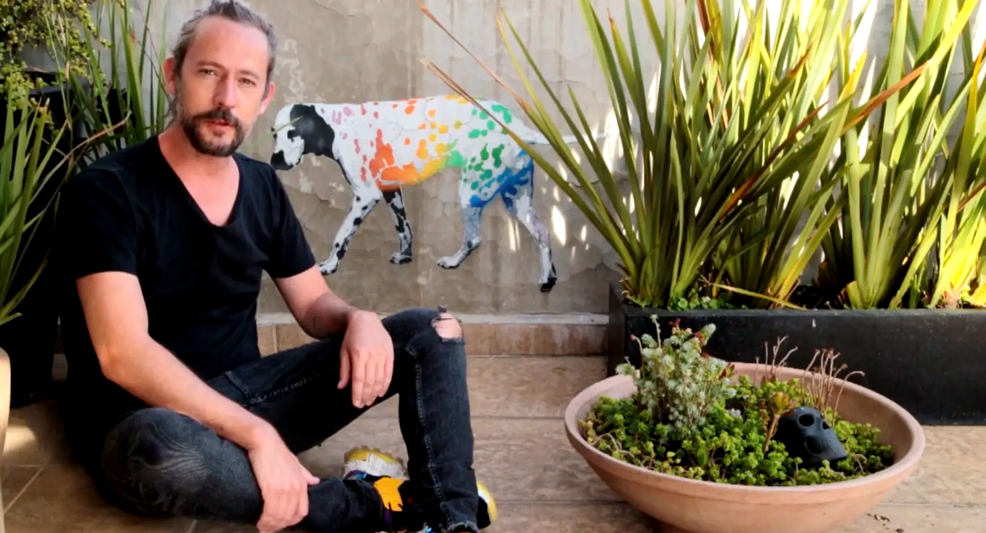 Muralist seated beside his rainbow-spotted dalmatian wall painting